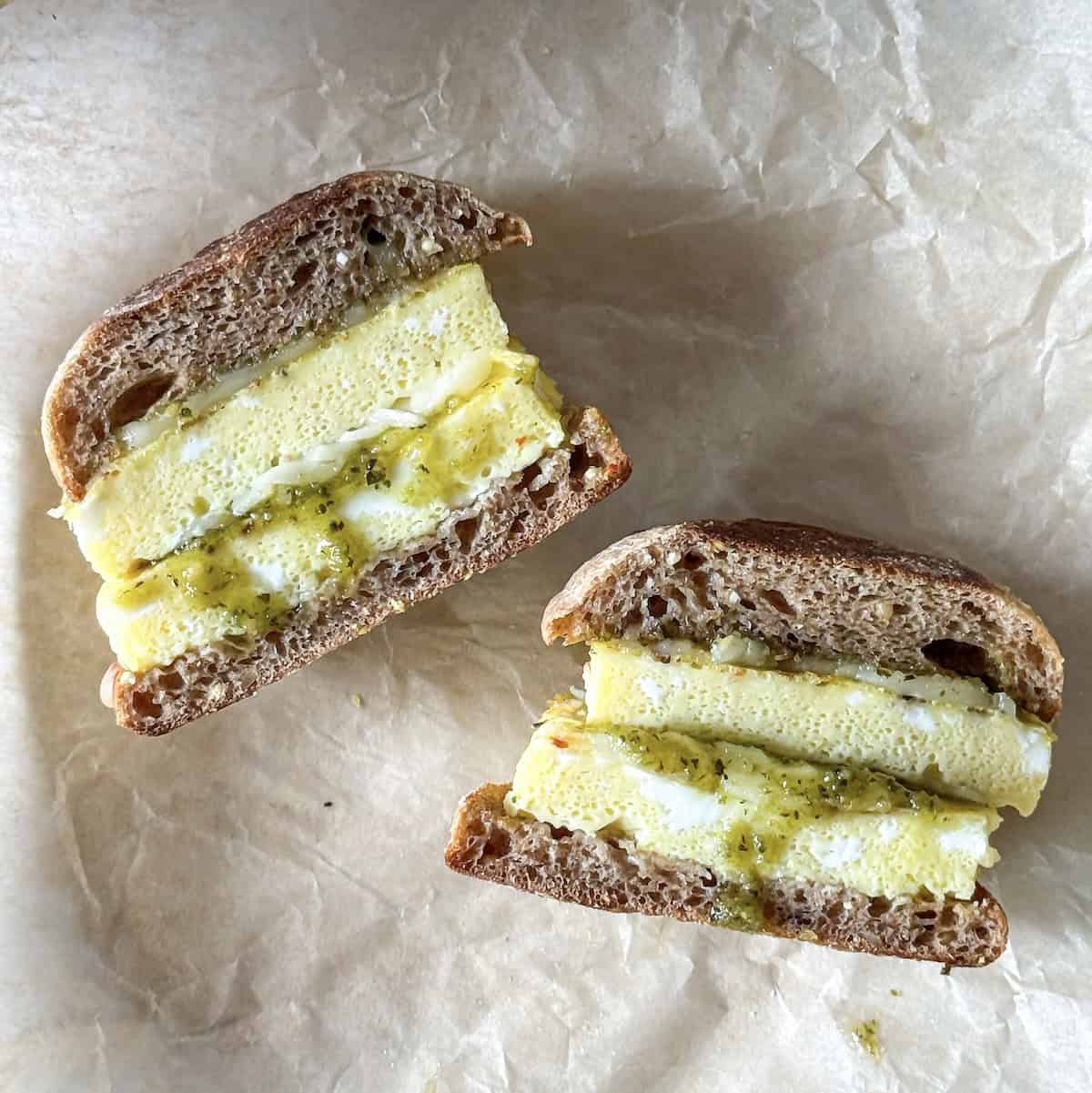 pesto egg sandwich cut in half on a parchment paper.
