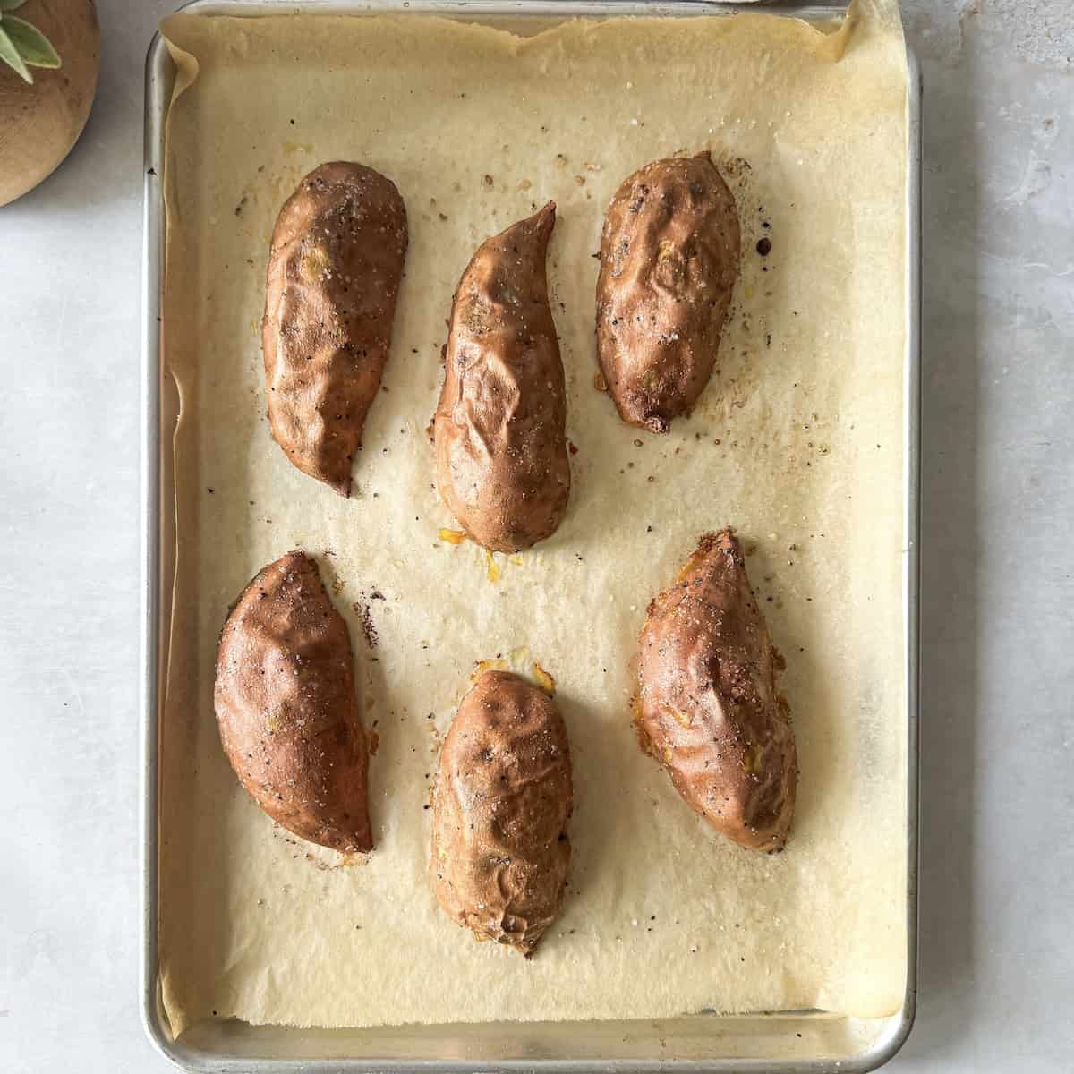 roasted sweet potato halves on a baking sheet overhead view before flipping.
