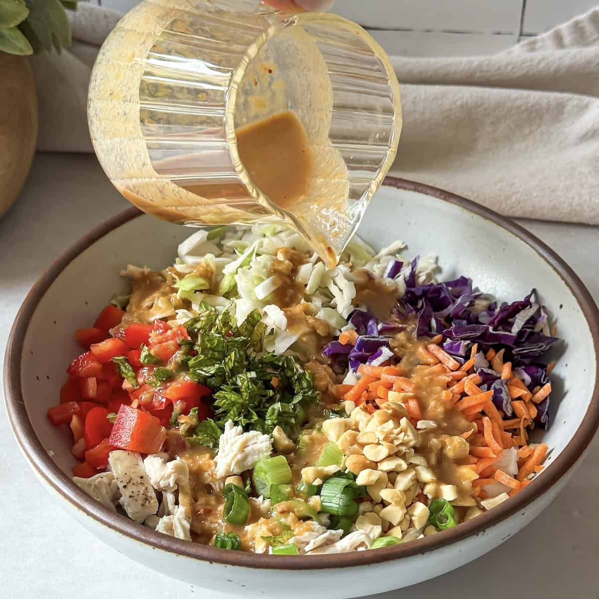 human hand pouring dressing on a thai chicken salad.