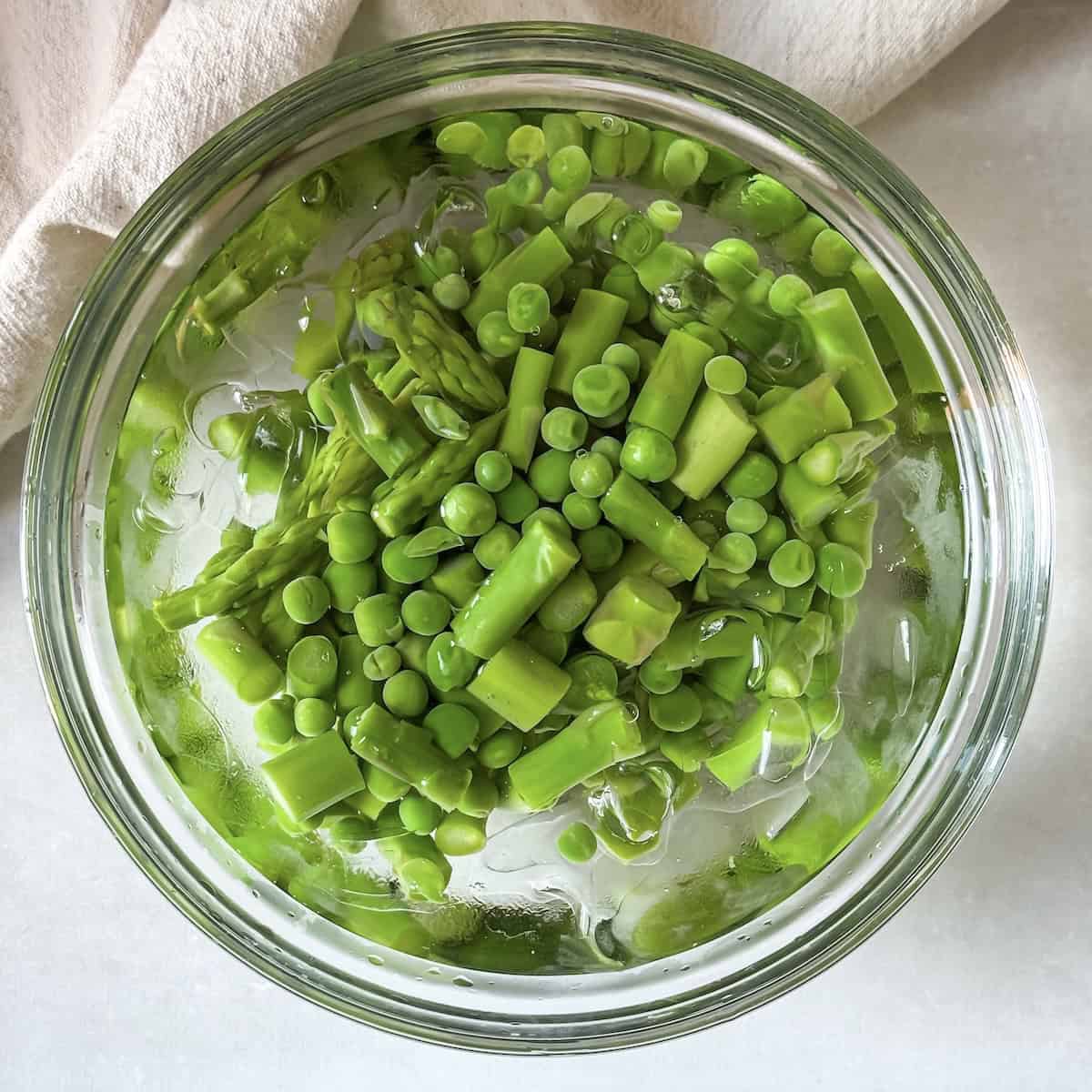 overhead view of asaparagus and peas in a bowl of ice water.