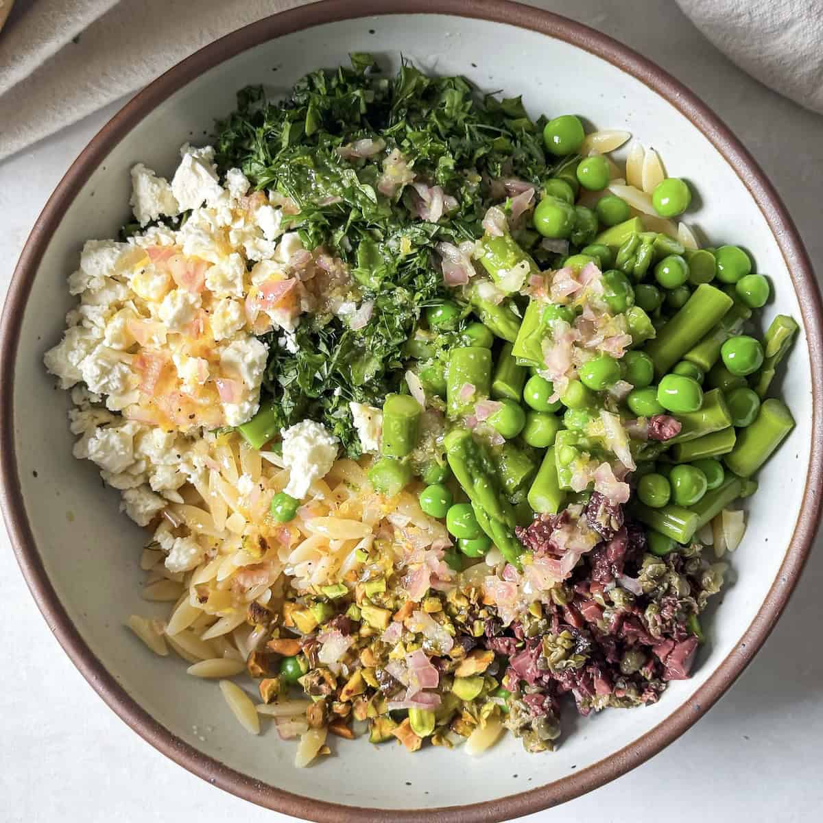 spring orzo pasta salad ingredients in a bowl before tossing.