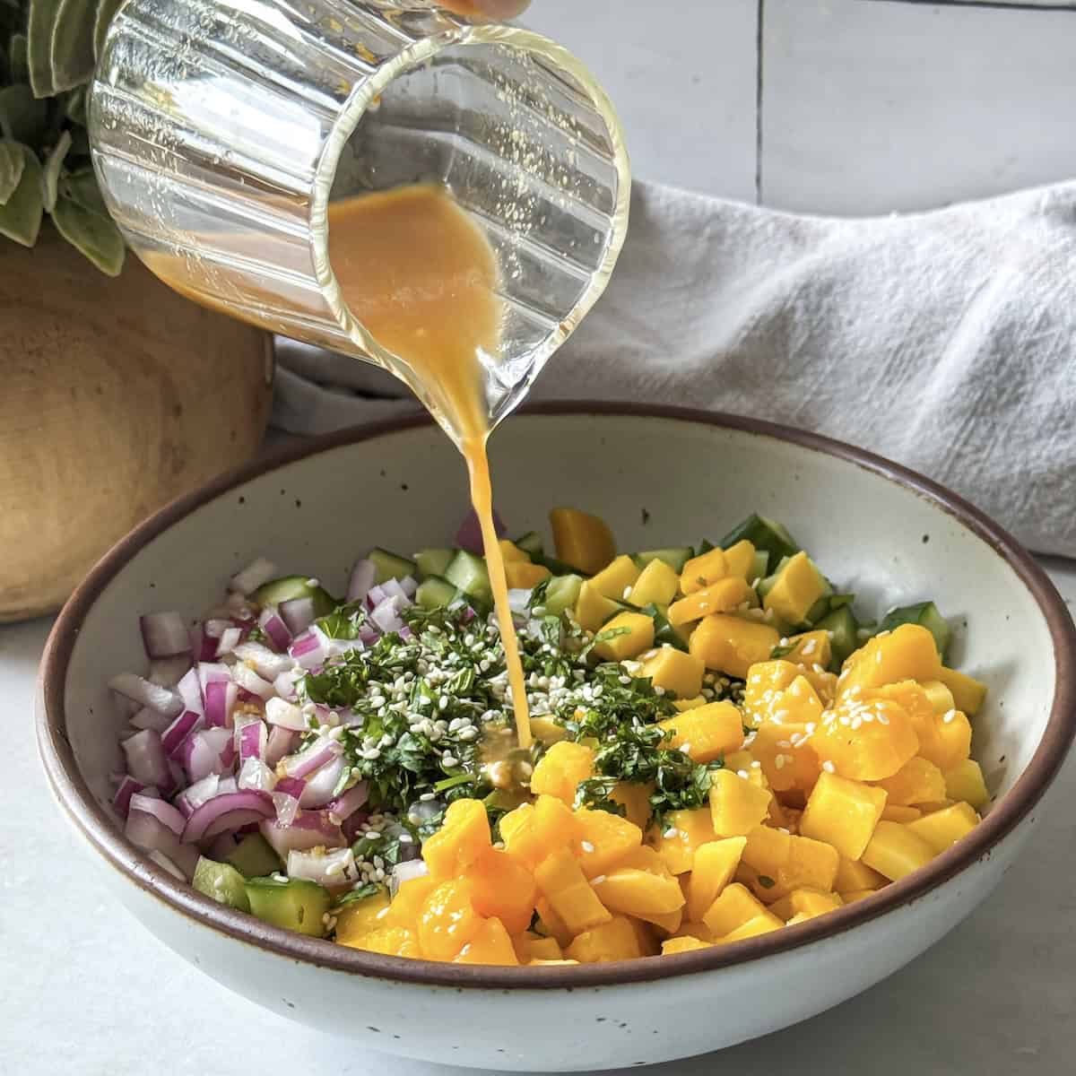 dressing being poured on cucumber mango salad.