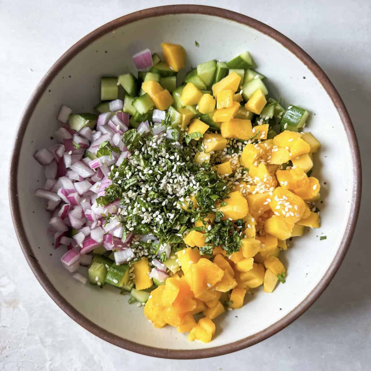 overhead view of cucumber mango salad ingredients in a bowl.