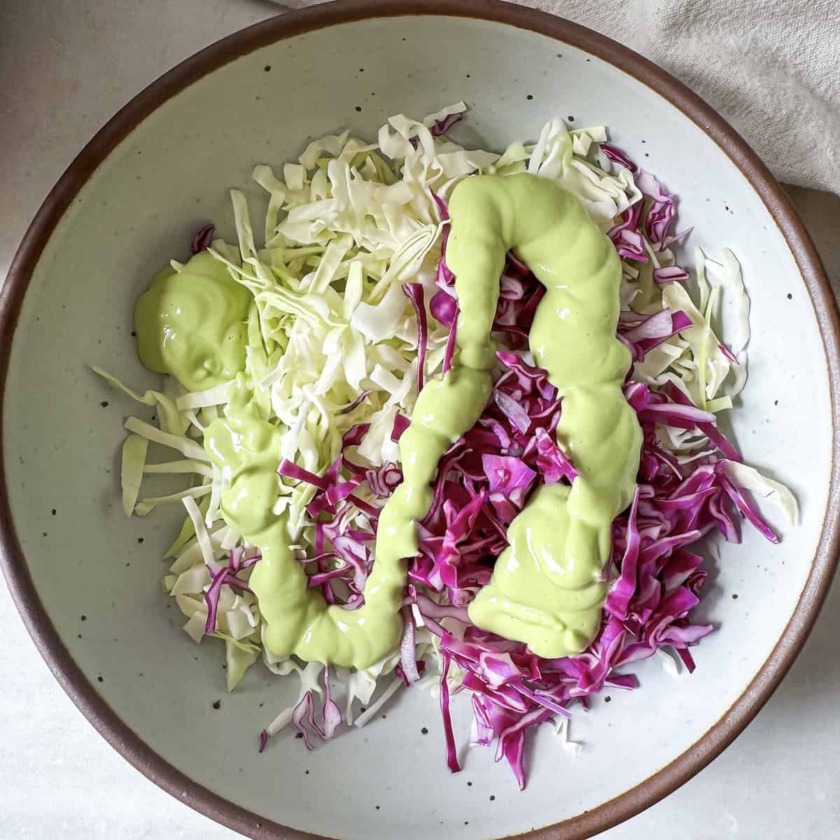 overhead view of avocado coleslaw with dressing added.