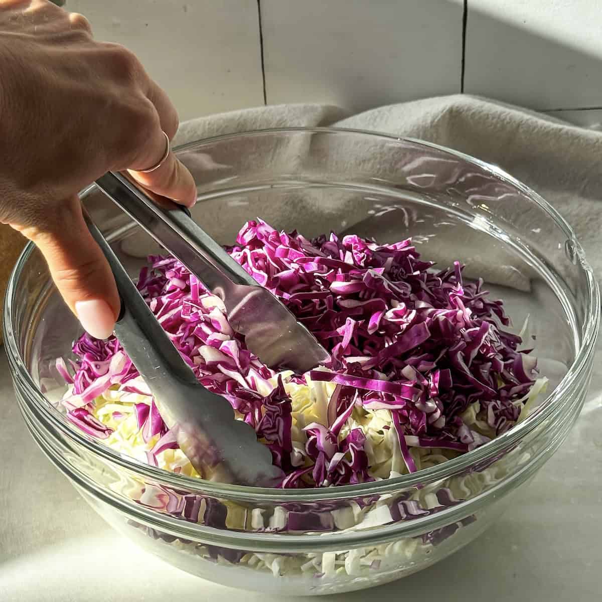 human hand mixing cabbage and dressing