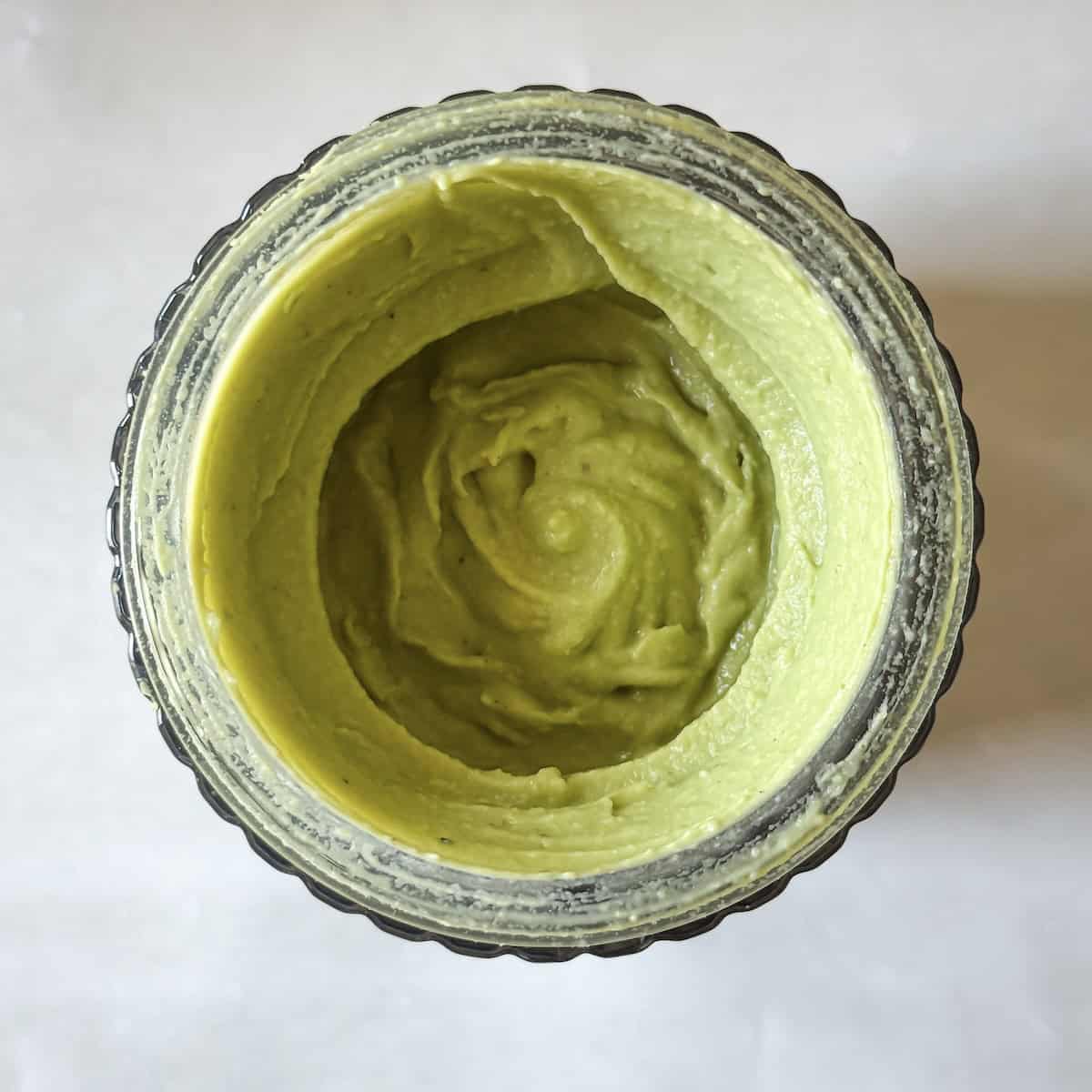 a thick green blend of white beans, dill, parsley, tahini, and seasonings in a glass blender.