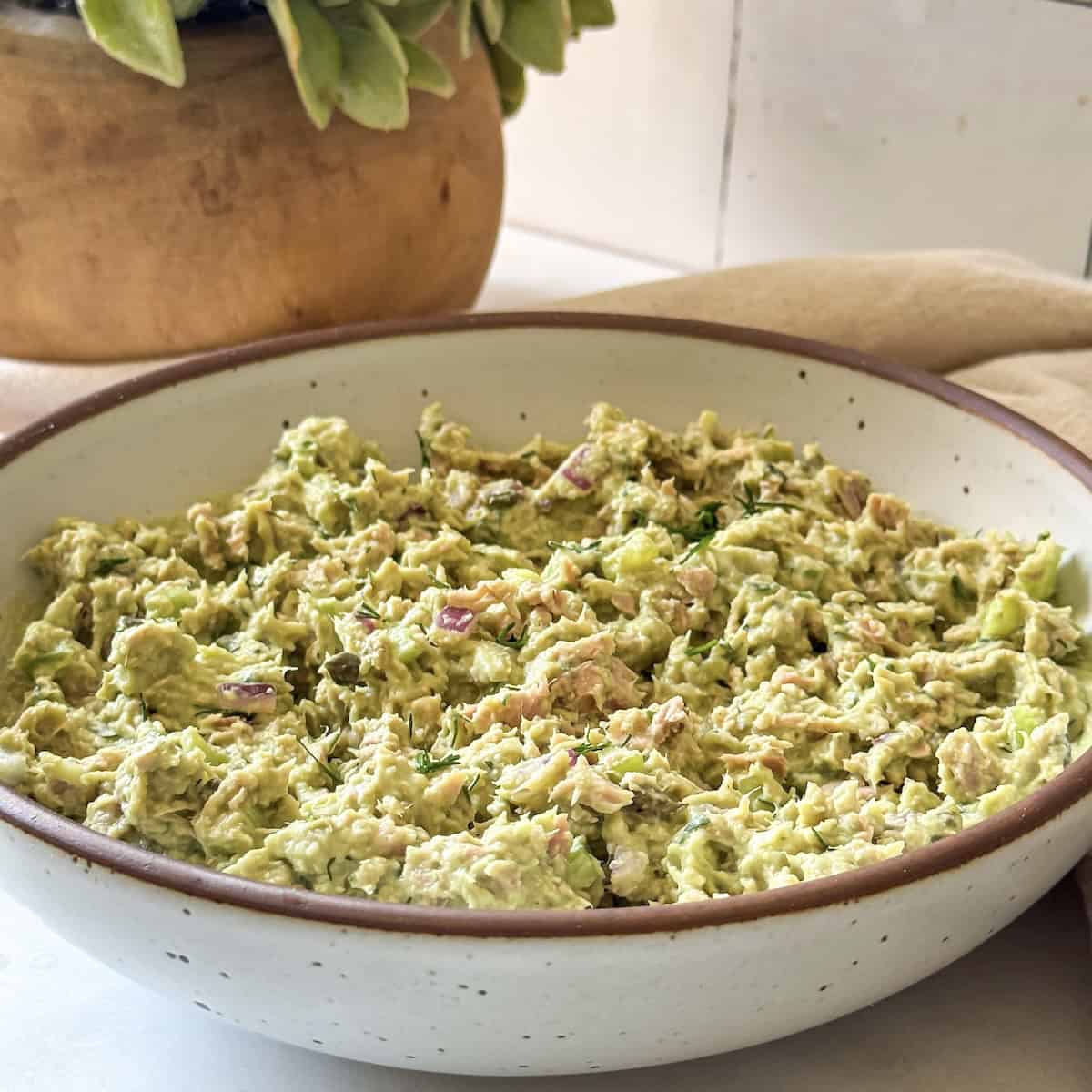 a white speckled bowl with a brown rim with a slightly vibrant green tuna salad after all the ingredients have been combined.