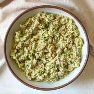 a white speckled bowl with a brown rim with a slightly vibrant green tuna salad after all the ingredients have been combined together.