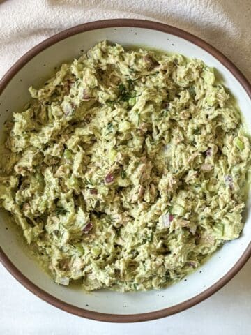 a white speckled bowl with a brown rim with a slightly vibrant green tuna salad after all the ingredients have been combined together.