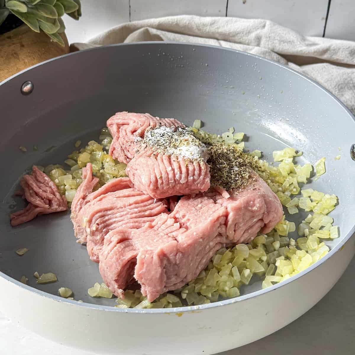 Ground turkey added to a skillet with seasonings on top before it's been broken apart.
