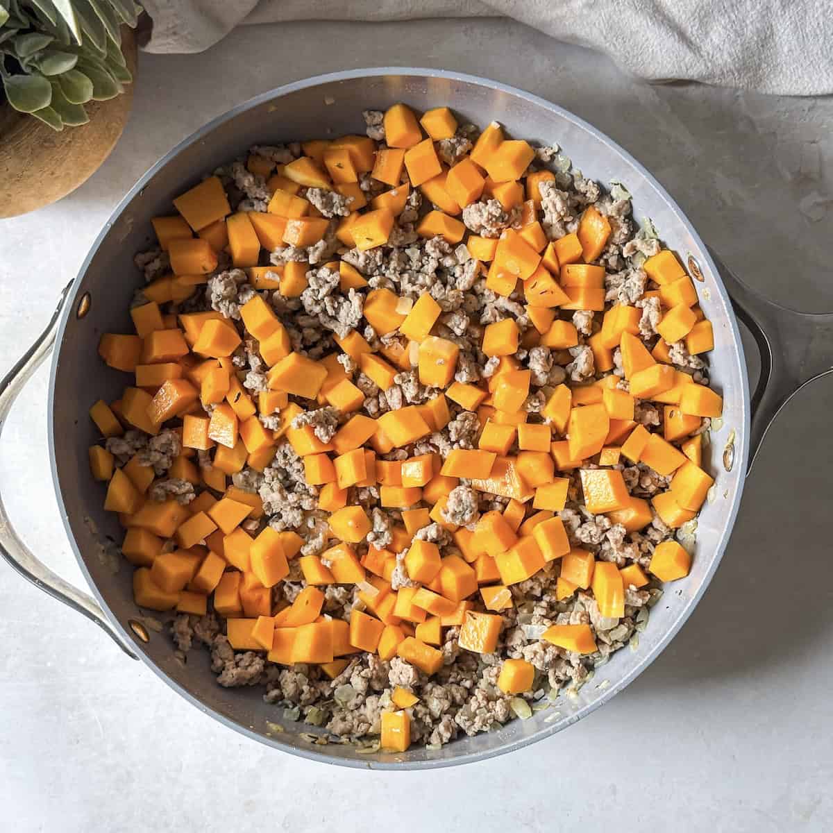 Cooked ground turkey with cubed butternut squash in a skillet.