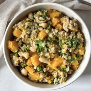 A white bowl with ground turkey butternut squash kale white bean skillet right after it's been cooked.
