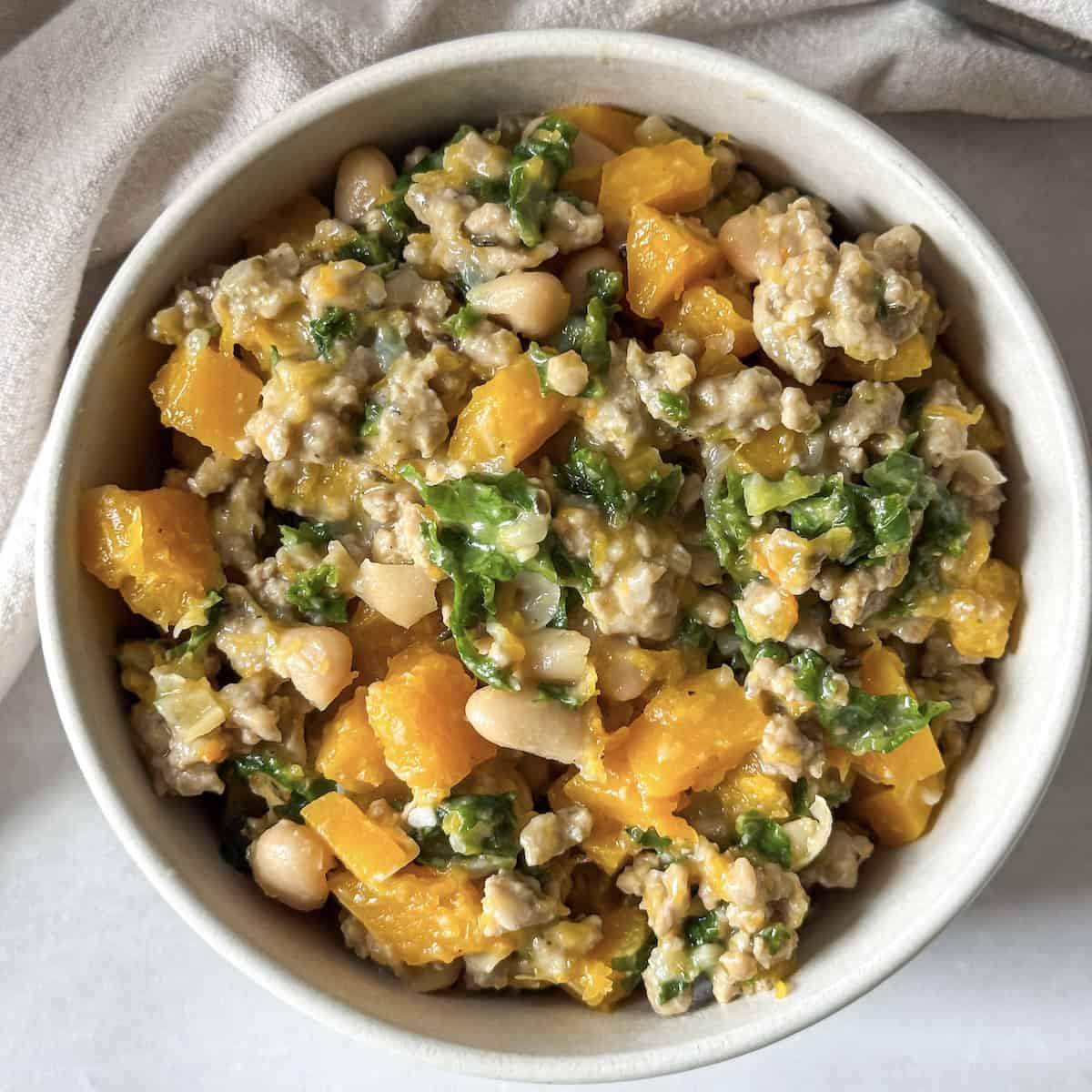 A white bowl with ground turkey butternut squash kale white bean skillet right after it's been cooked.