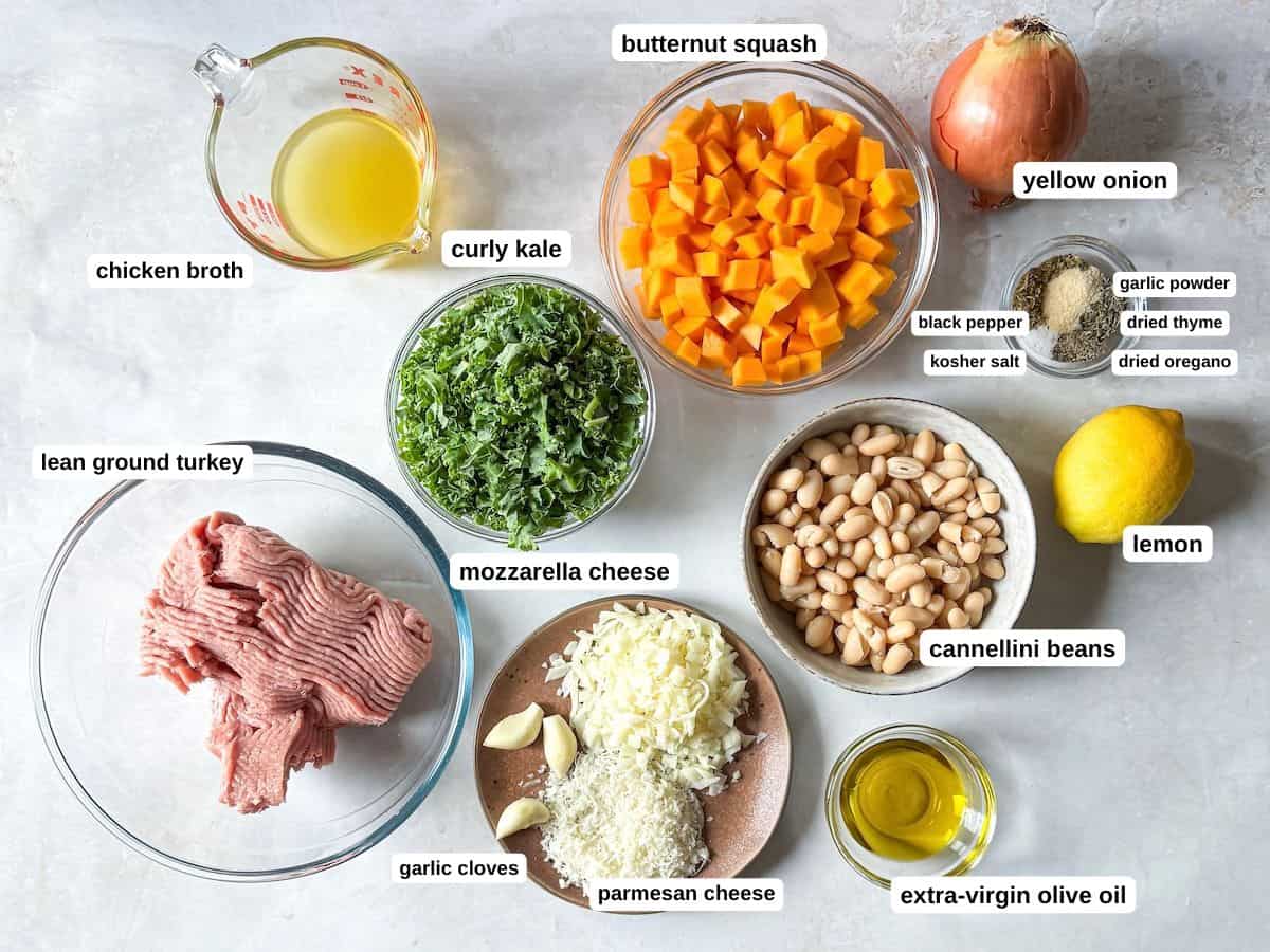 Ingredients to make a turkey, butternut squash, kale, white bean skillet dinner in separate containers on a whitish gray background with labels.