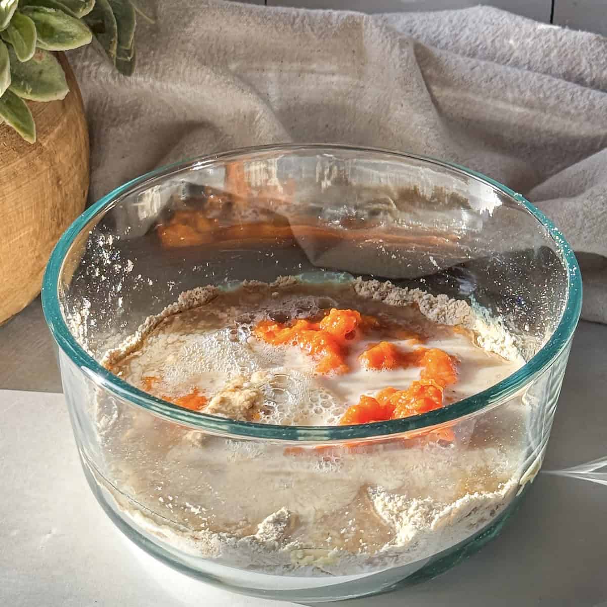 Wet ingredients including orange pumpkin puree and almond milk added to the dry ingredients to make pumpkin protein pancake bowls in a glass bowl.