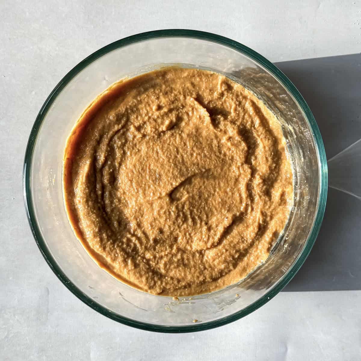 a burnt orange colored pancake batter in a glass bowl with a grayish white background.