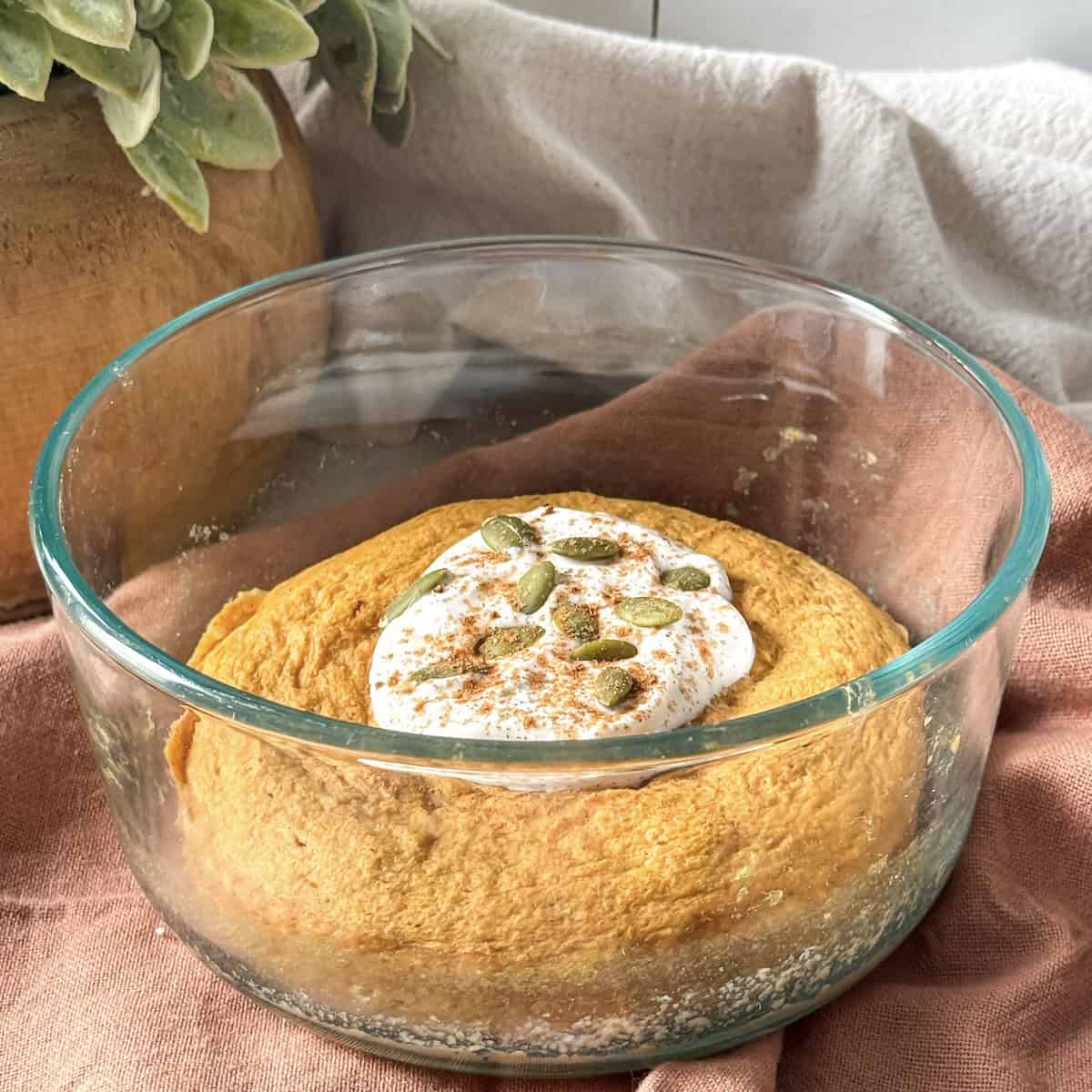 a pumpkin protein pancake bowl after being cooked in a glass bowl with a scoop of greek yogurt, pumpkin seeds, and pumpkin pie spice on top..