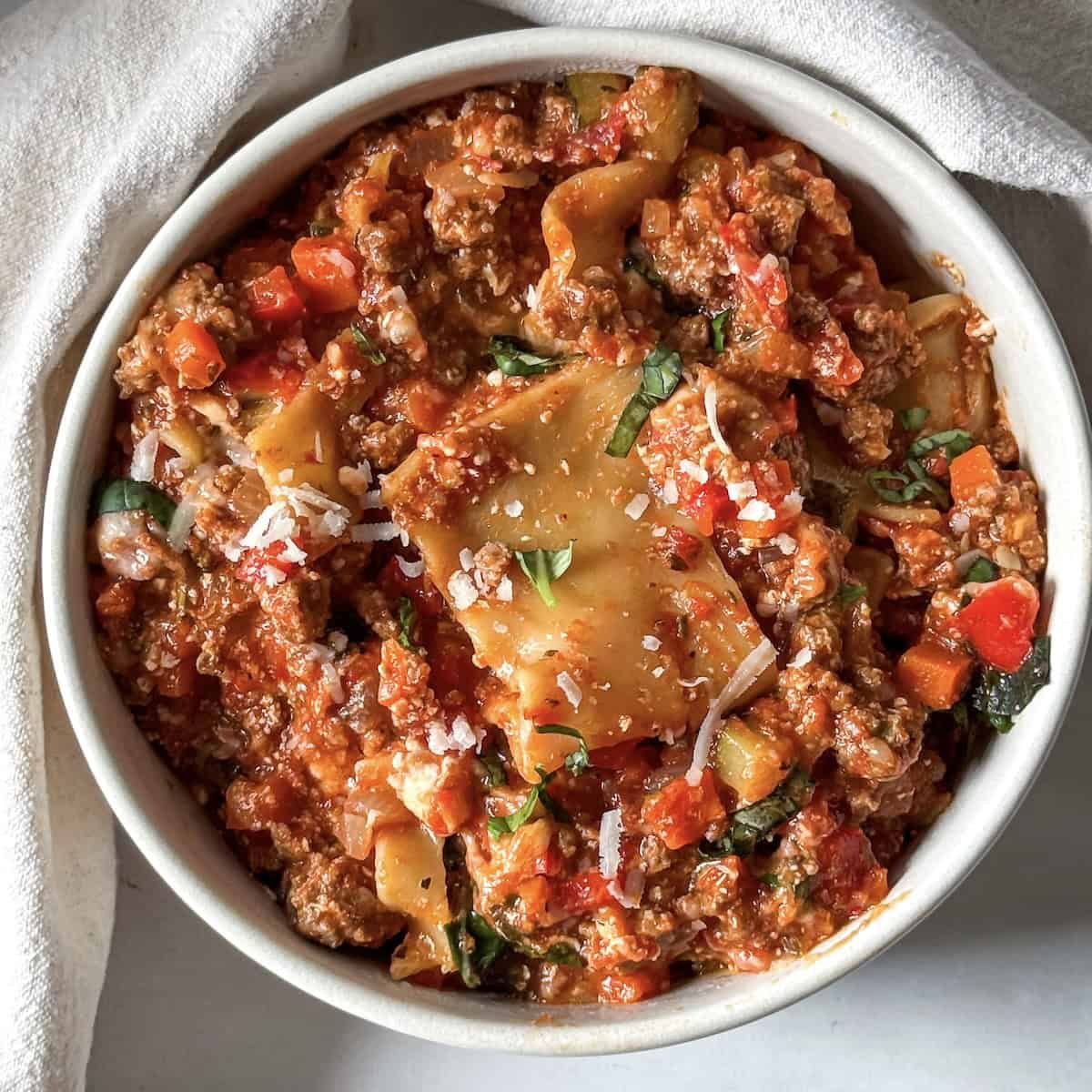 a white bowl with lasagna skillet dinner topped with basil.