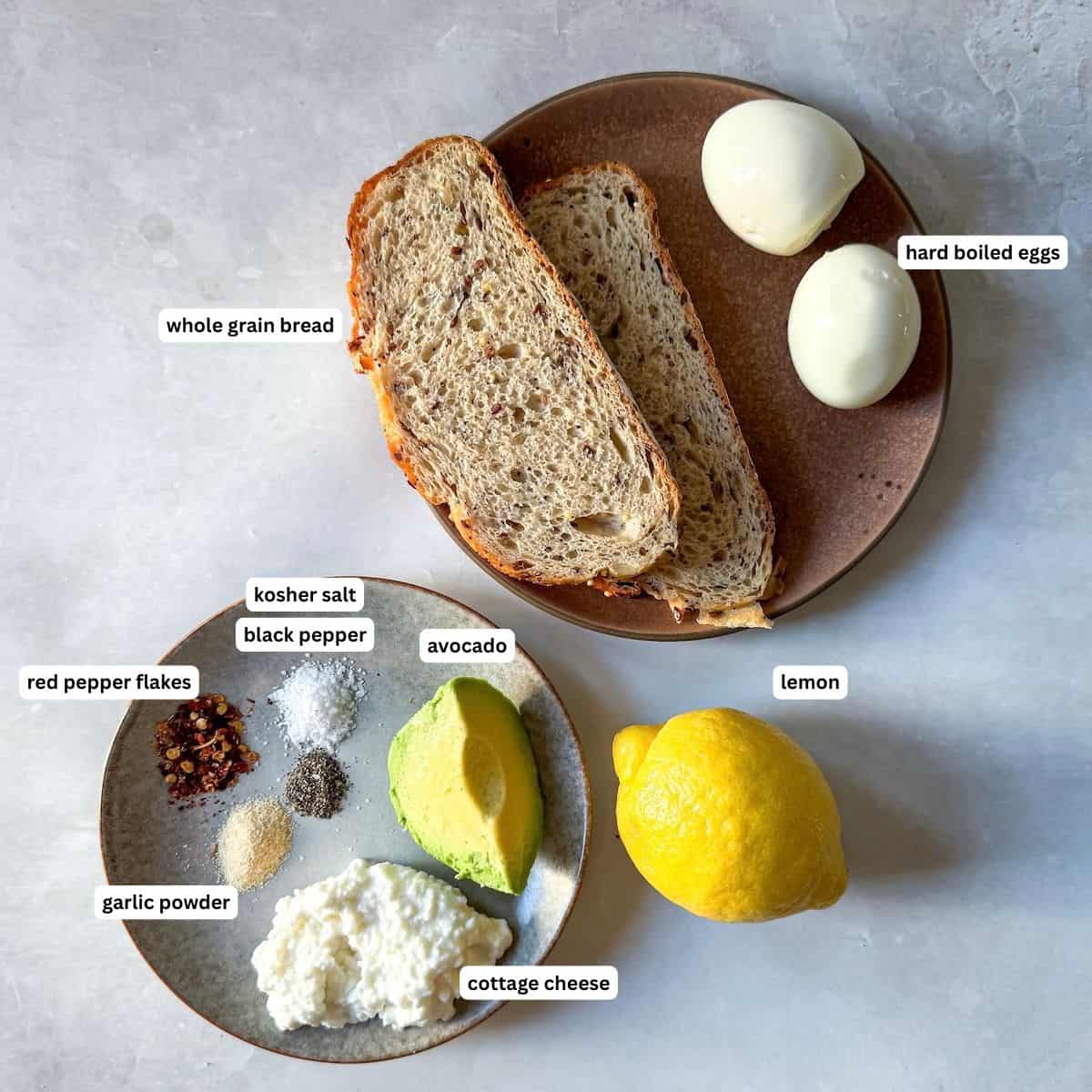 avocado toast with cottage cheese and egg ingredients lableled on a table with a grayish white background.