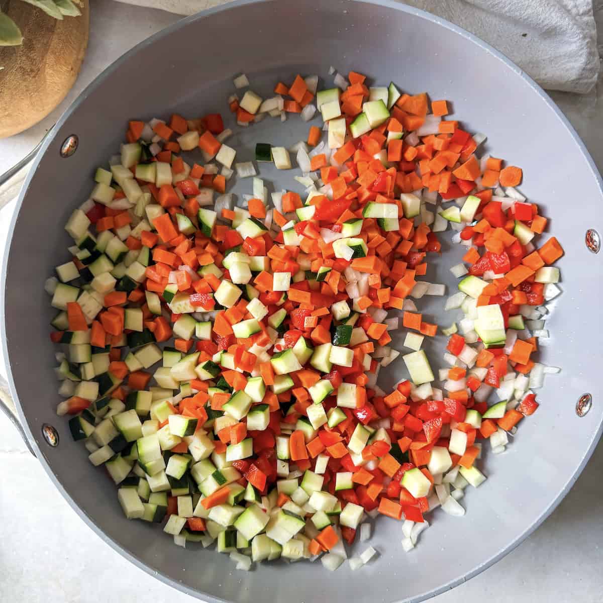 carrots, red pepper, zucchini, and yellow onion in a skillet right before being cooked.