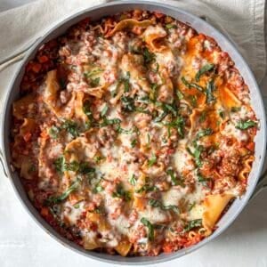 Cooked lasagna skillet right after mozzarella, basil, and parmesan have been added and cooked.