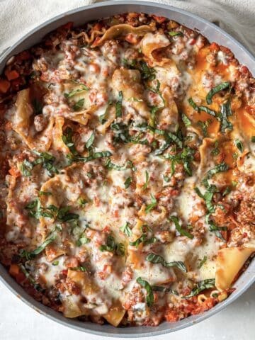 Cooked lasagna skillet right after mozzarella, basil, and parmesan have been added and cooked.