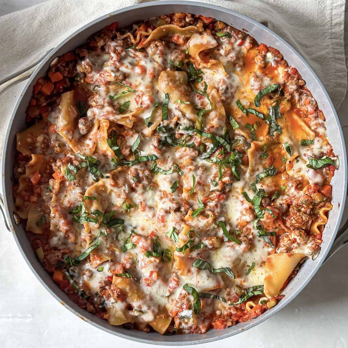 Cooked lasagna skillet right after mozzarella, basil, and parmesan have been added and cooked.