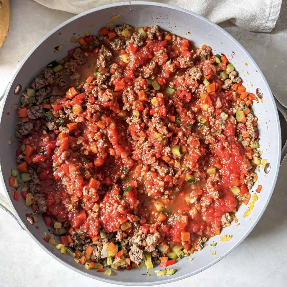 crushed tomatoes added to ground beef and cooked veggies in a large skillet.