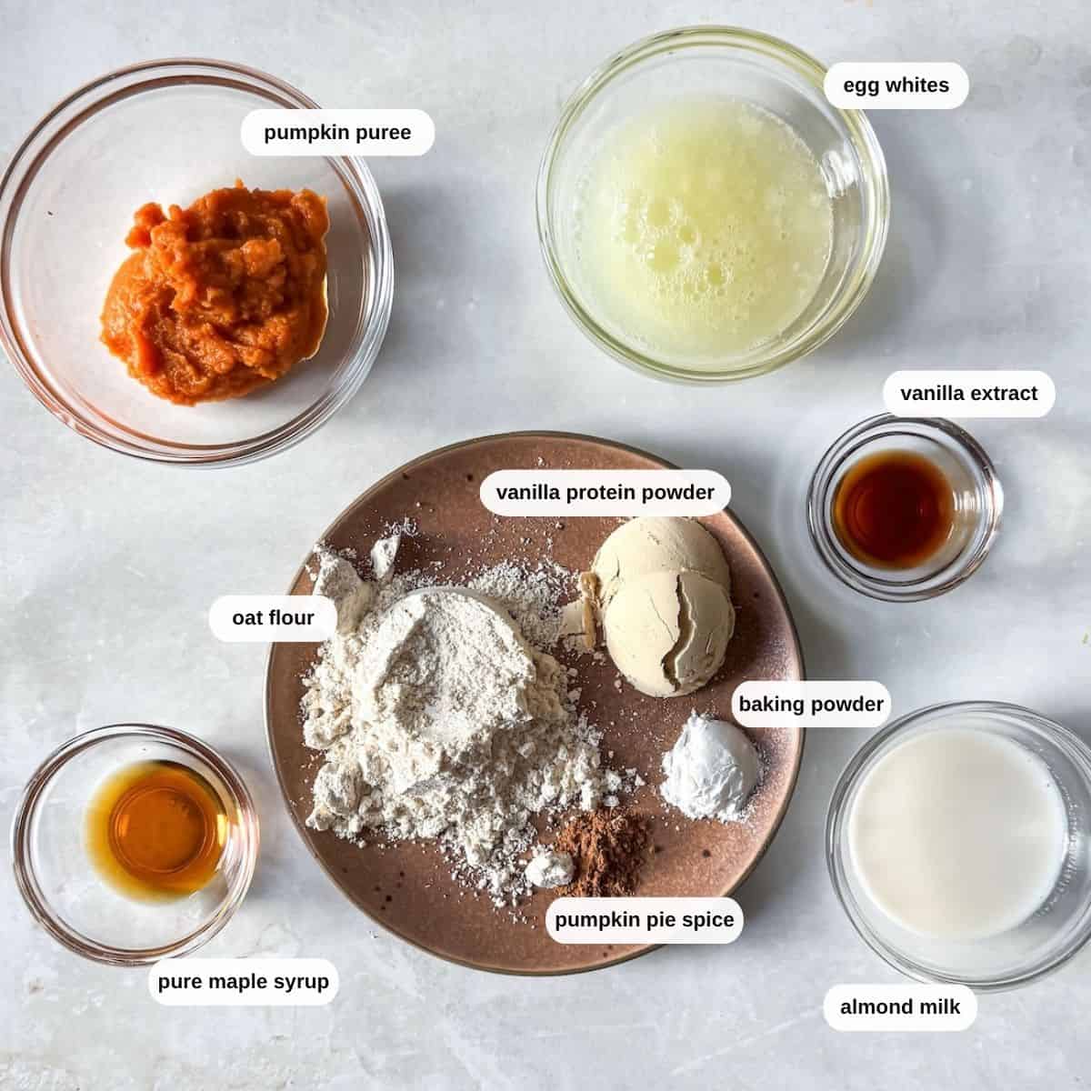 ingredients for pumpkin protein pancake bowls on a table in their own individual bowls on a grayish white background.