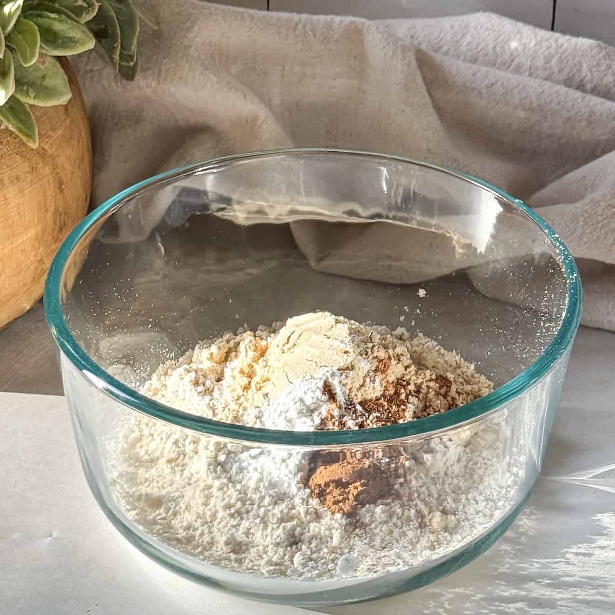 the dry ingredients used to make a pumpkin protein pancake bowl in a glass bowl with a tan dishcloth in the background.