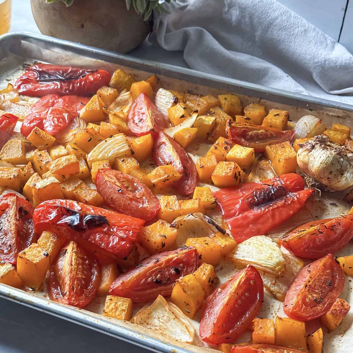 Diced butternut squash, roma tomatoes, bell pepper, yellow onion, and garlic on a sheet pan lined with parchment paper right after coming out of the oven.