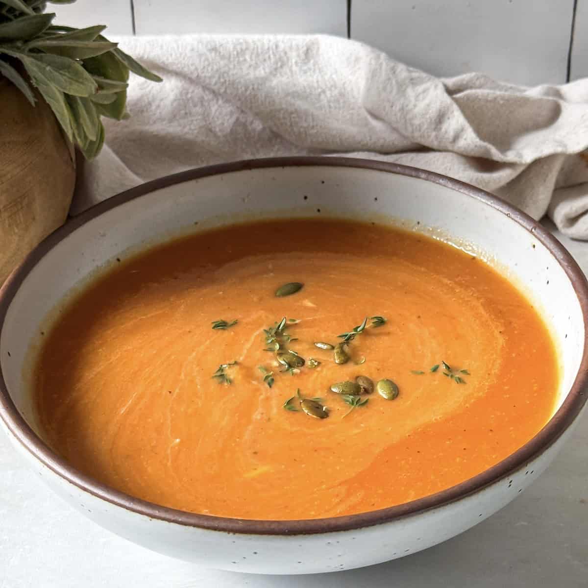 butternut squash tomato soup in a bowl right after being cooked. It's topped with fresh thyme and a swirl of Greek yogurt.