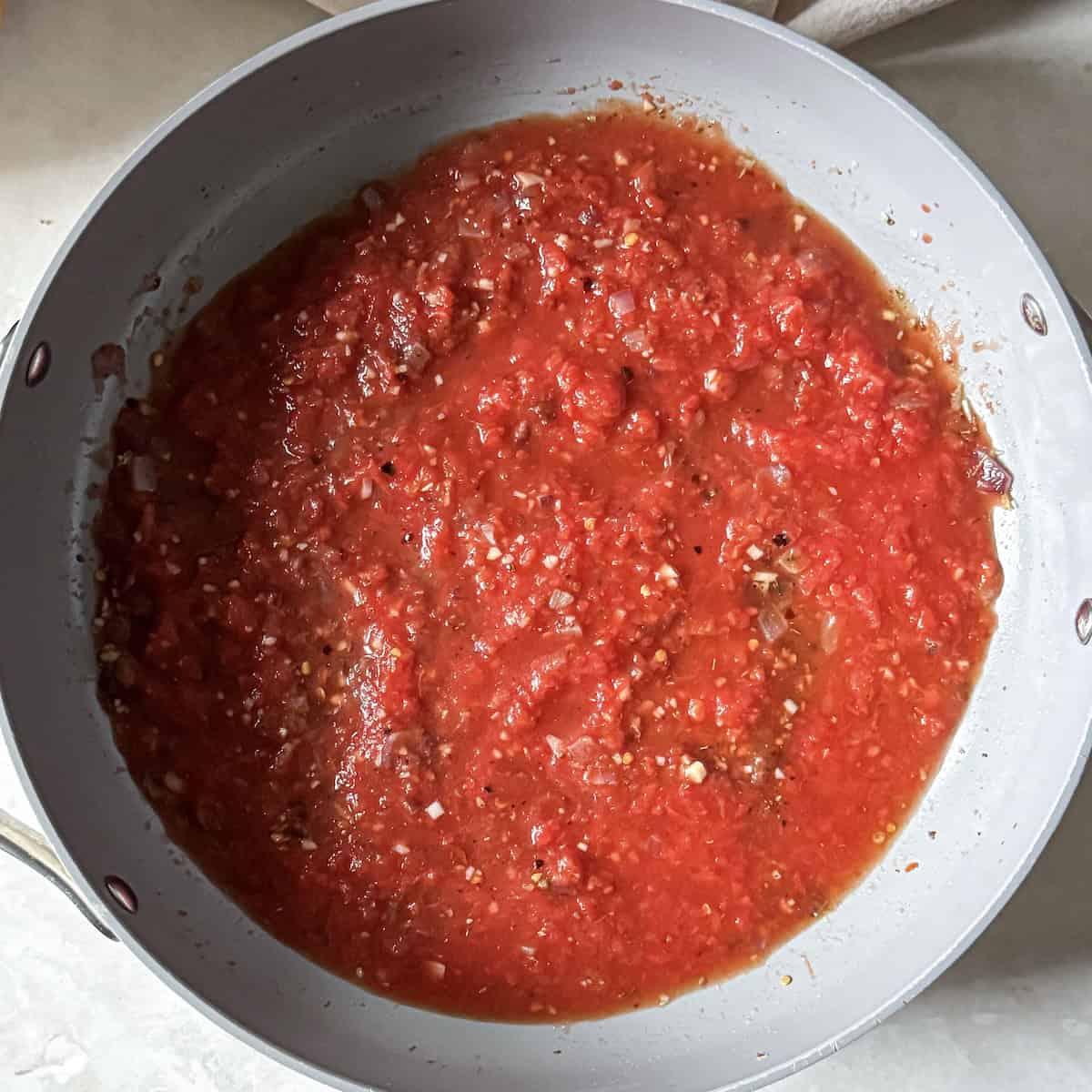 Crushed tomatoes added to red onion and garlic in a skillet.