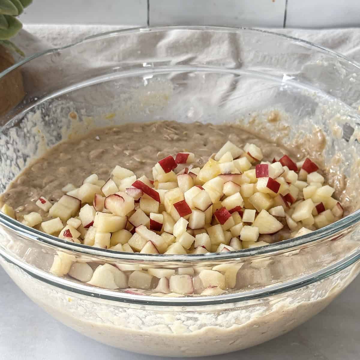 Diced apples added to a glass bowl with the muffin batter.