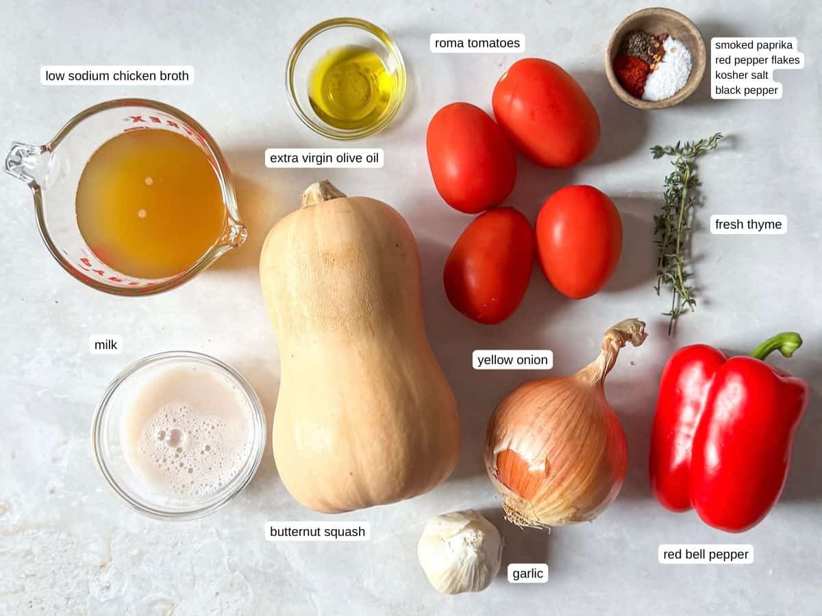 ingredients for Butternut Squash Tomato Soup in separate containers labeled on a table with a grayish white background.