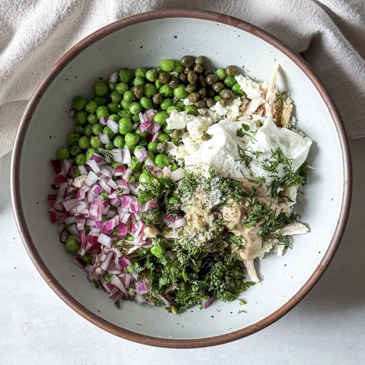 ingredients for chicken salad with peas in a bowl before being mixed together.