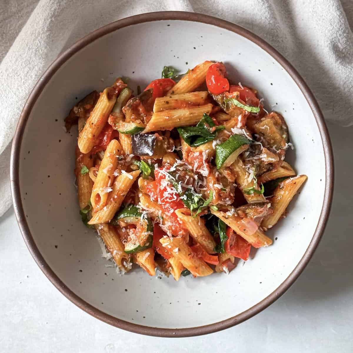 roasted vegetable pasta in a bowl with freshly shredded parmesan on top.