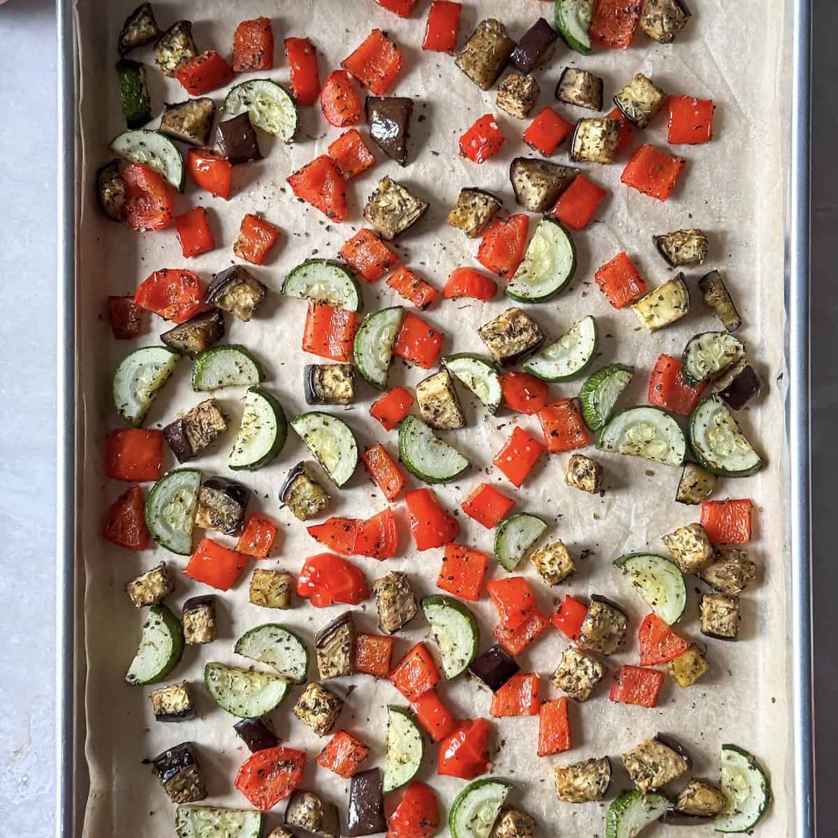 Roasted zucchini, red bell pepper, and eggplant on a sheet pan.